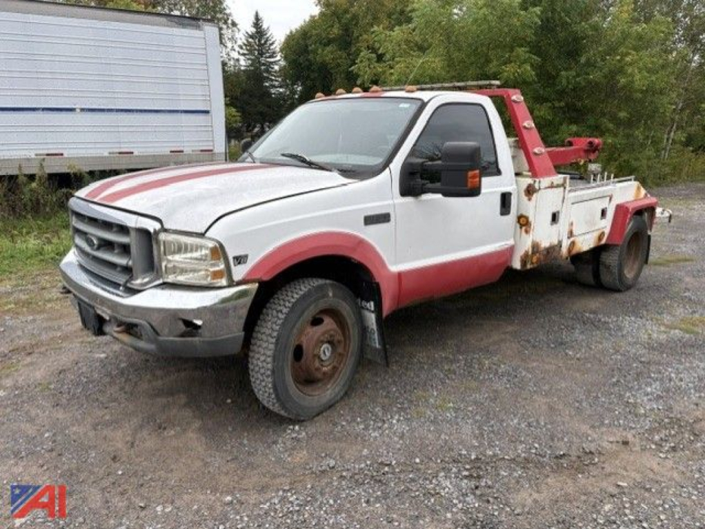 1999 Ford F-450 tow truck front-left view showing white body with red accents and rust on wheel wells and tow equipment.
