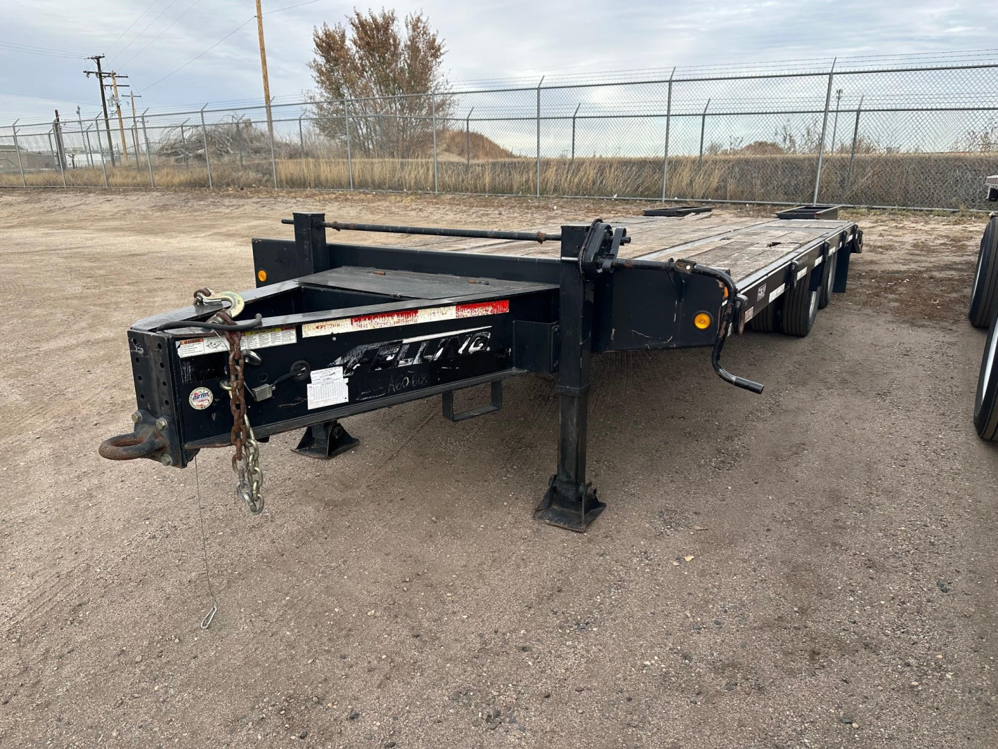 Flatbed trailer showing hitch and deck with black frame and multiple wheel wells.
