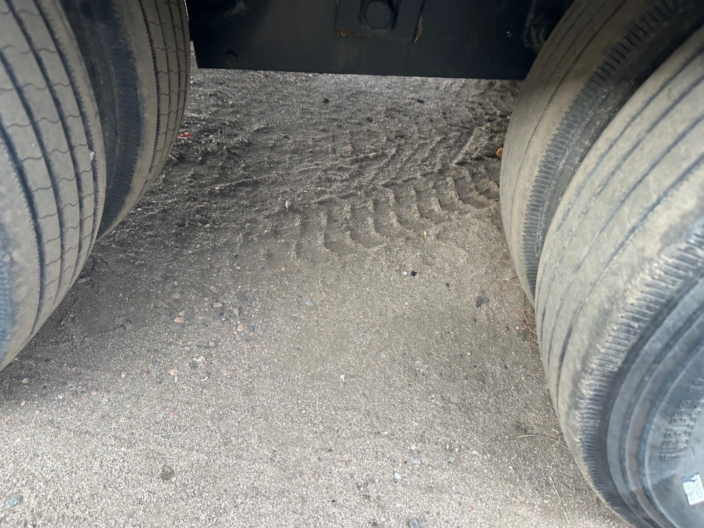 Trailer axle area showing dual tires and road grime in the gap under a flatbed trailer.