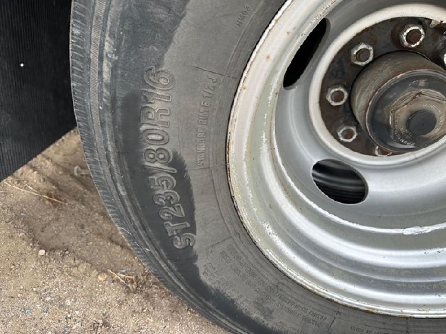 Trailer wheel with tire showing tire markings and wheel hub. Visible text includes tire size S F225/80R16 and wheel lug pattern surrounding center.