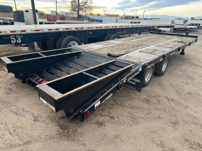 Flatbed trailer showing loading deck with metal ramps and dual axles in a used condition.