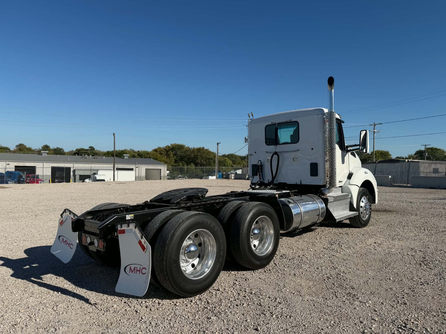 Kenworth T880 conventional daycab tractor rear view showing dual rear axles and fuel tanks, white cab, gravel lot.