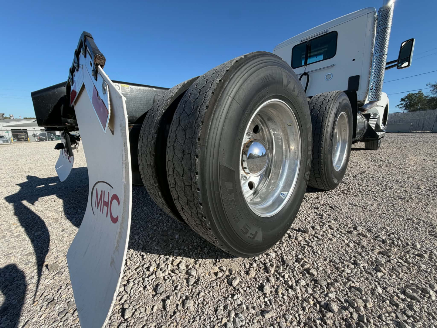 Kenworth T880 rear view showing dual rear axles and tire tread, white cab, gravel lot.