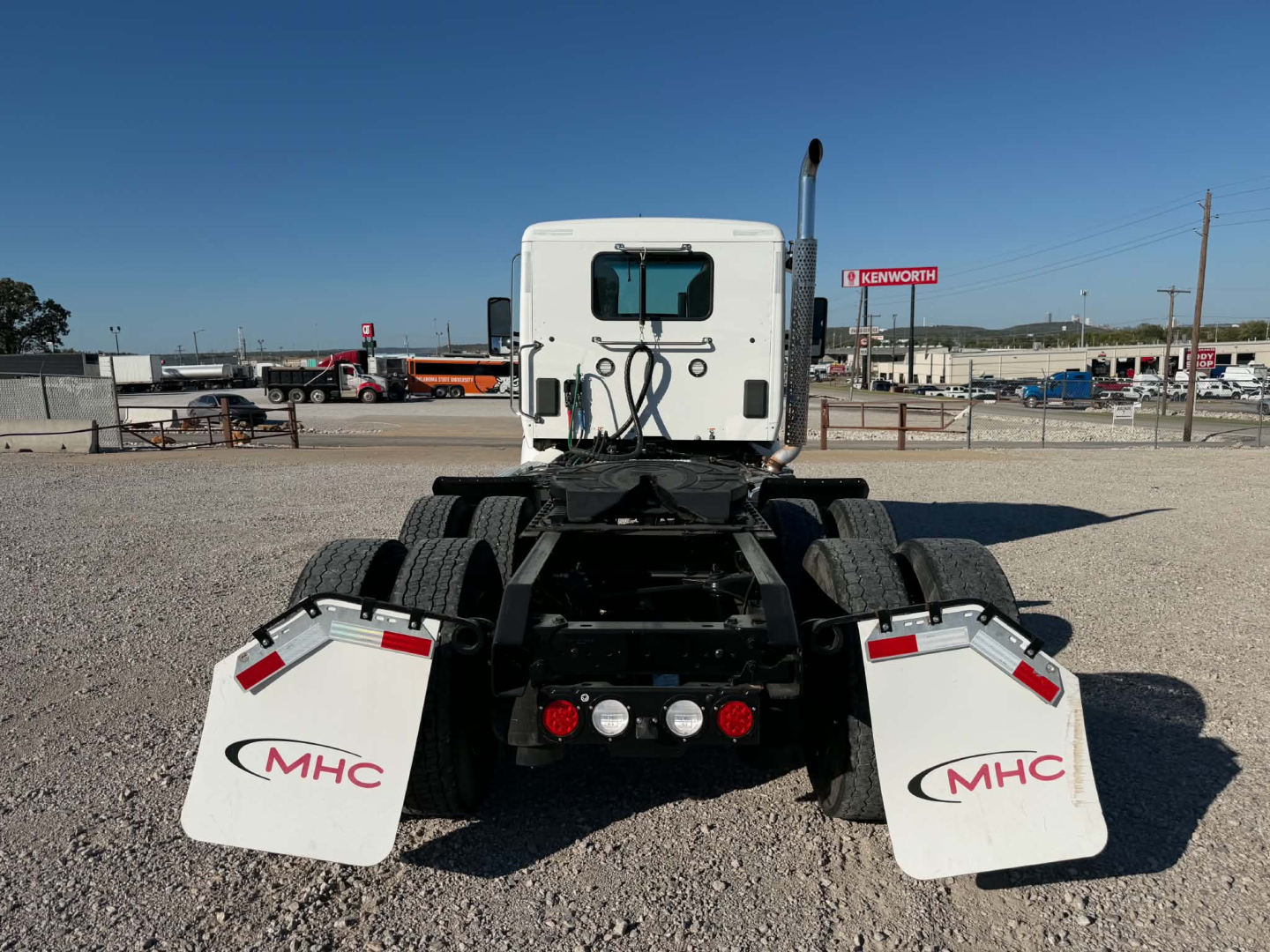 Rear view of 2022 Kenworth T880 chassis showing dual rear axles, white cab, mud flaps with MHC logo, and spare area for fifth wheel.