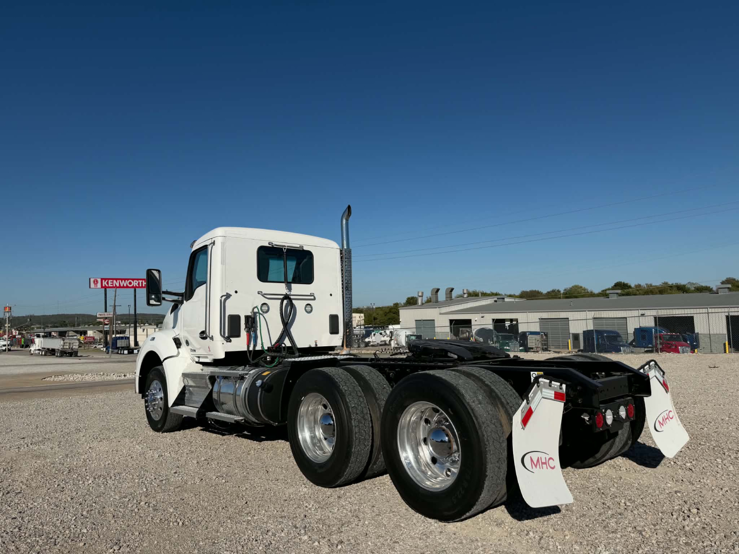 Kenworth T880 tractor rear view showing triple rear axles and white mud flaps with MHC logo.
