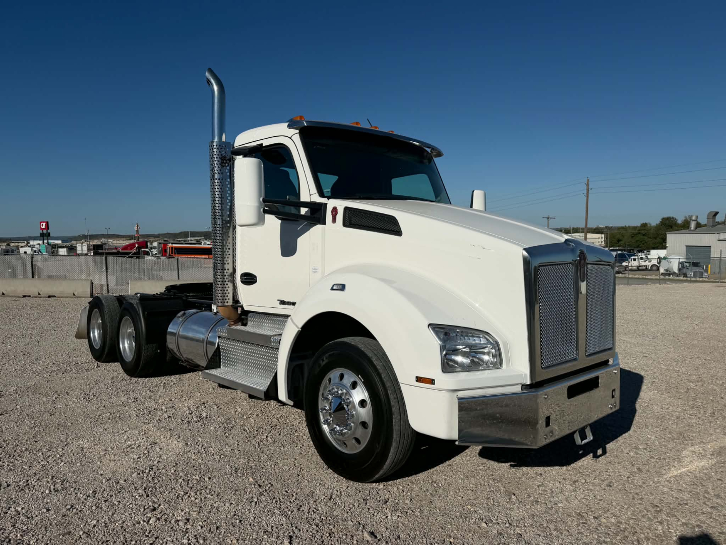 Kenworth T880 heavy-duty truck in a yard, white, with chrome exhaust stack, grille and bumper. Side view shows front wheel, cab, and dual rear axles. No visible text on image.