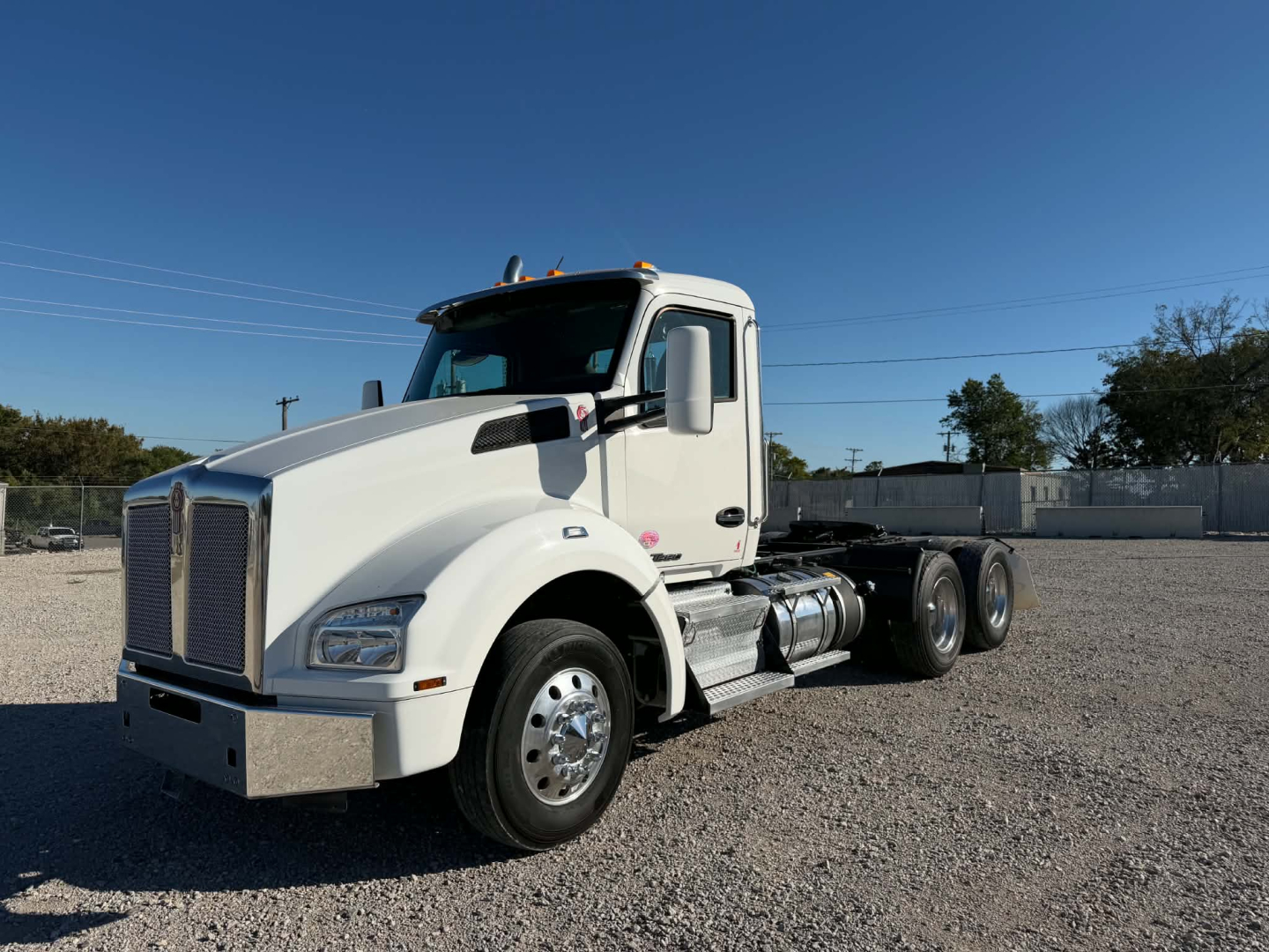 Kenworth T880 conventional daycab truck in white, front-left view, chrome bumper, large grille, dual rear axles, fuel tanks visible, clear blue sky.