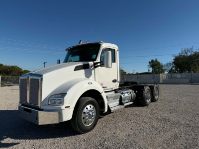 Kenworth T880 conventional daycab truck in white, front-left view, chrome bumper, large grille, dual rear axles, fuel tanks visible, clear blue sky.