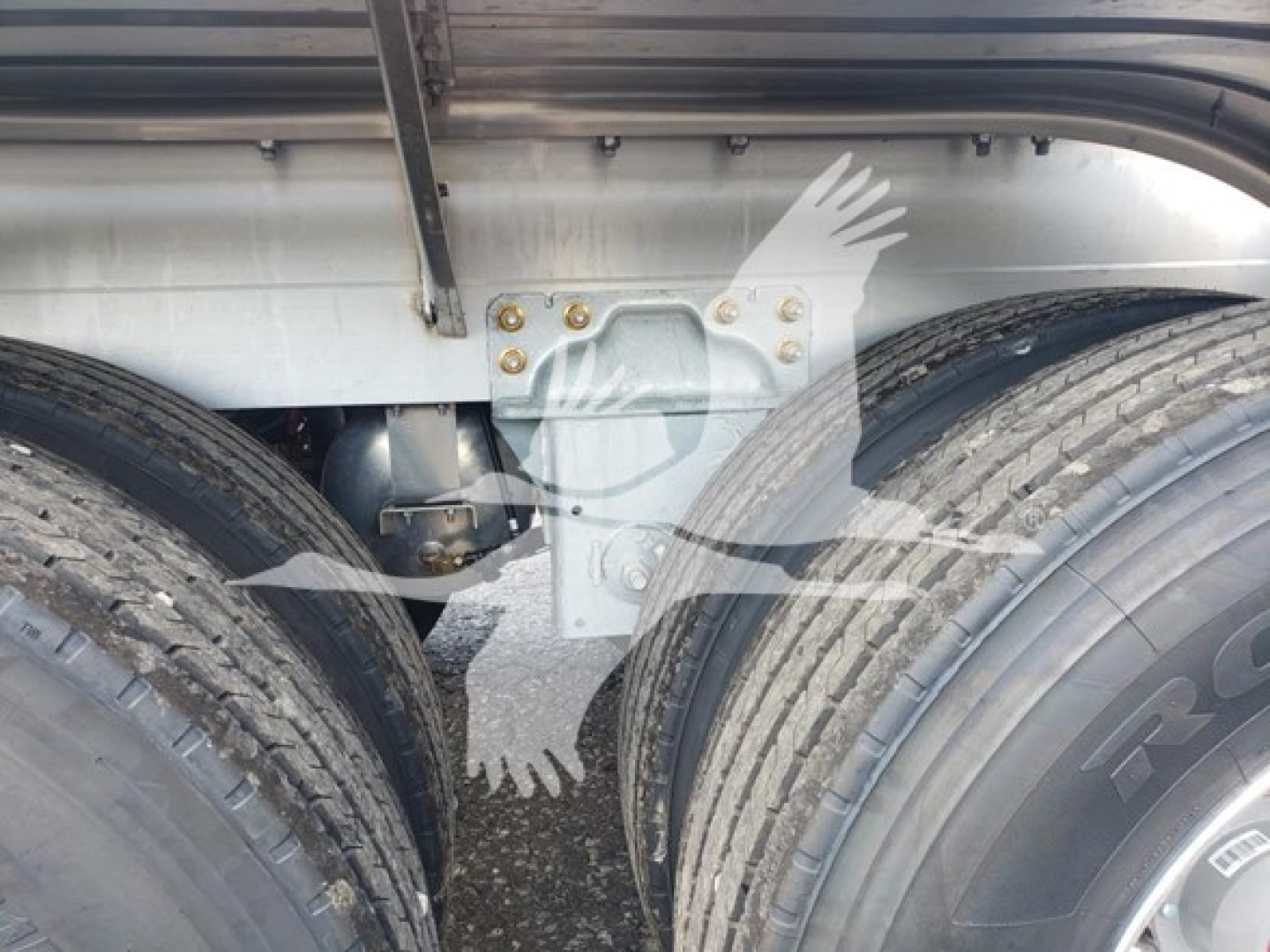 Dual rear axles of a Heil 406A Petro trailer with visible suspension brackets and tire treads; metal frame and bolts present.