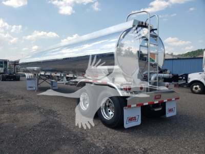 Heil 406A Petro tanker trailer in a dealership lot showing polished cylindrical tank, rear dual-axle with white mud flaps, ladder rack, and safety rails.