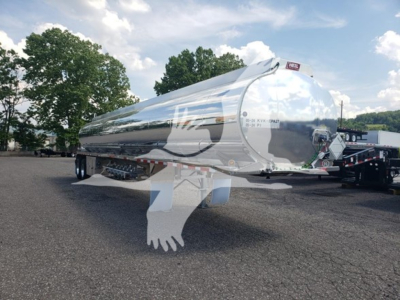 Trailer: polished aluminum Heil 406A Petro tanker trailer in yard, rear door and dual axles visible, reflection on body, set against trees and cloudy sky.