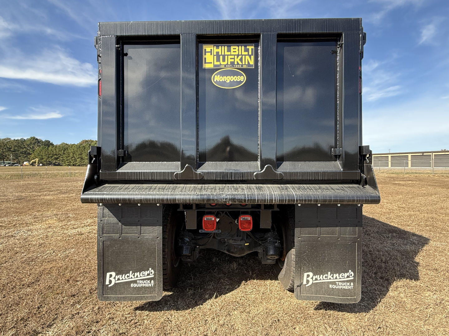 Dump truck bed rear view showing Mack GR84F new with black hull, Haliburton Lufkin Mongoose sticker, rear bumper, red taillights, and Bruckner mudflaps.