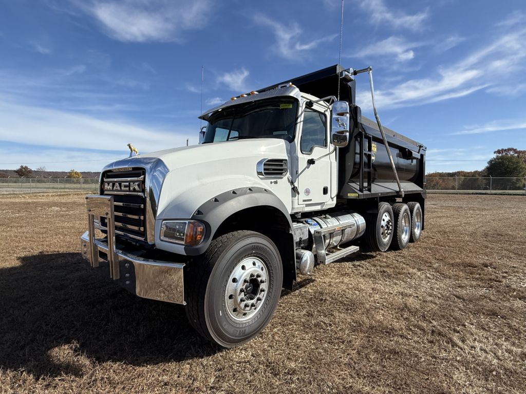 Mack GR84F dump truck in a field, front three-quarter view showing white cab, black dump bed, chrome bumper and dual rear axles.