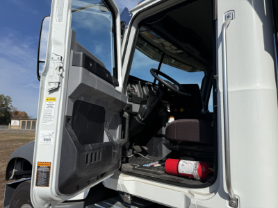 Truck cab interior of a 2026 Mack GR84F shown from open driver door with steering wheel, dashboard, and fire extinguisher visible.