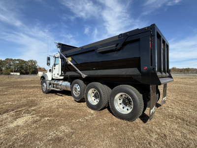 Truck bed with dump body on a white Mack GR84F chassis, side view showing three rear axles, black dump body, hydraulic hoist, clear sky