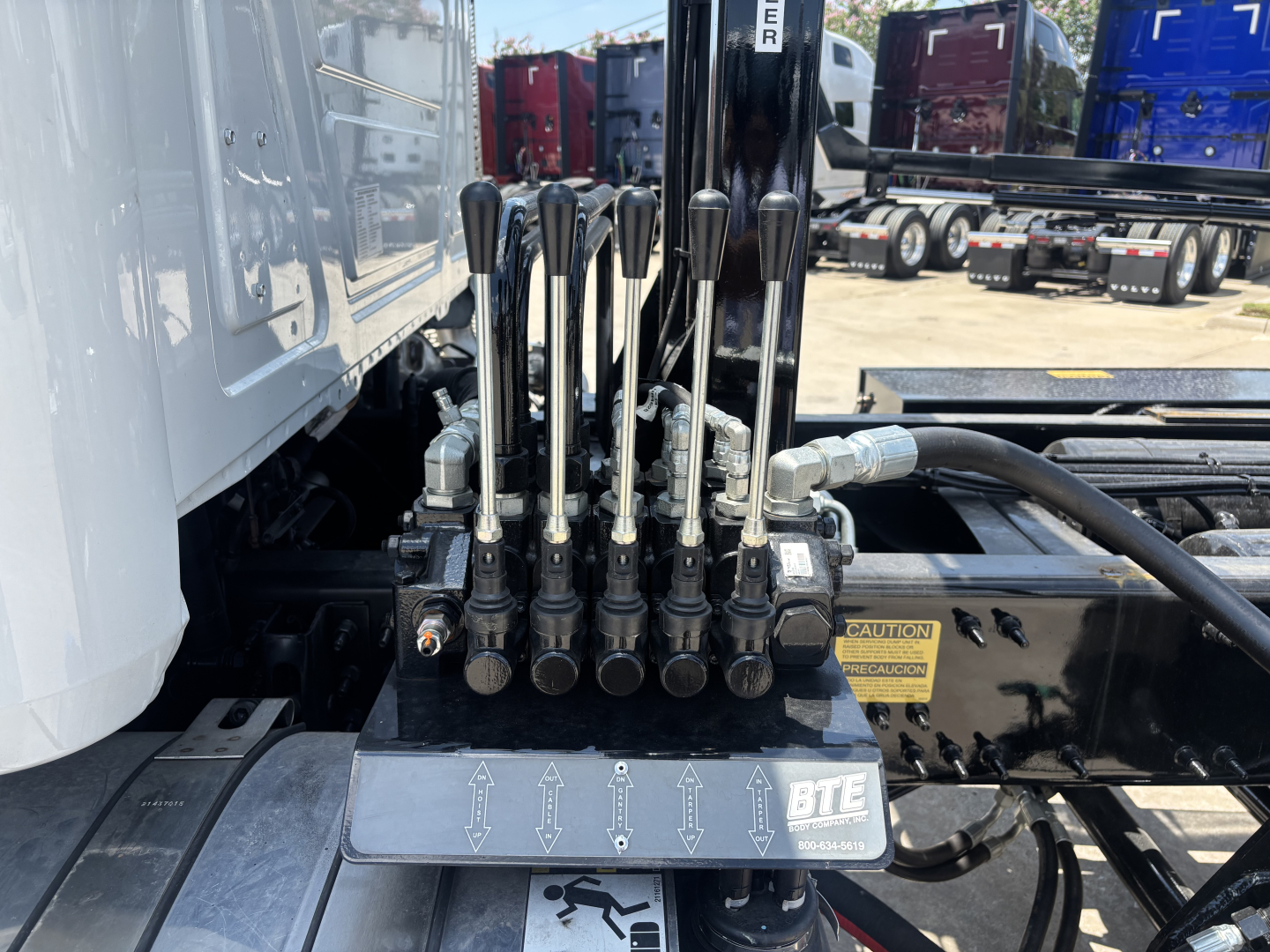 Hydraulic control levers for a Mack GR64B roll-off truck with multiple levers and hydraulic lines visible; buttons and labels on a metal plate show arrows and the BTE logo.