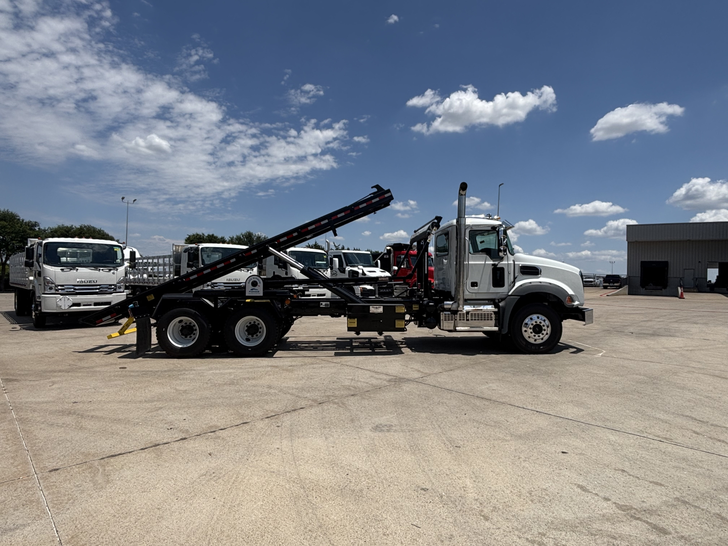 2026 Mack GR64B rolloff truck in an outdoor lot showing side profile with hydraulic arm and metal ramp.