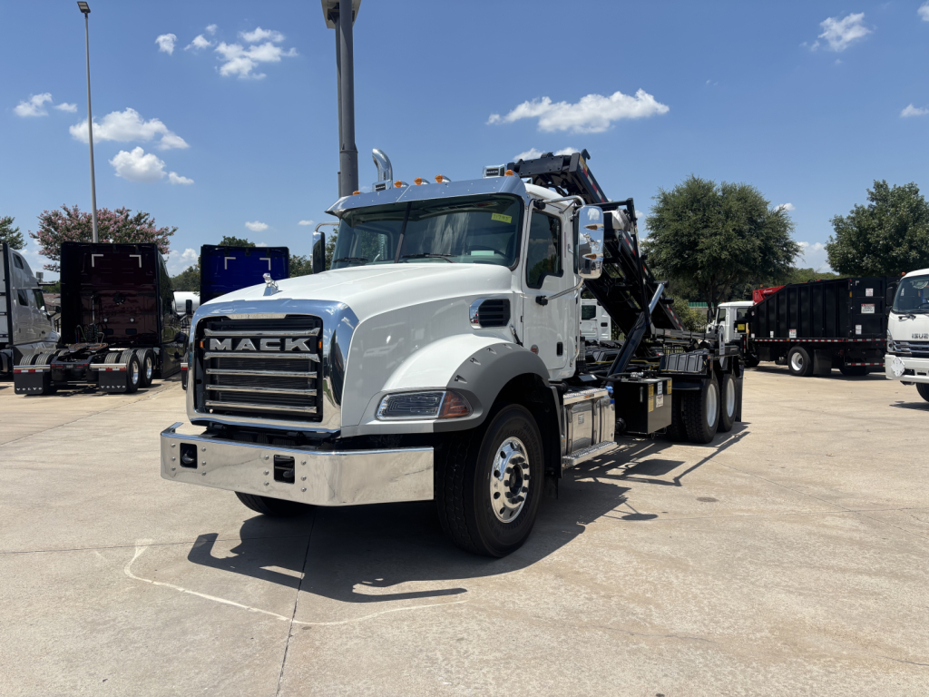 Mack GR64B rolloff truck in a parking lot showing chrome front bumper and crane/rolling bed with black hydraulic arms.