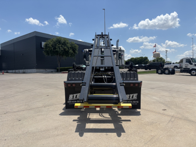 Truck bed and hydraulic arm of a new 2026 Mack GR64B roll-off truck, seen from rear in a dealership lot.
