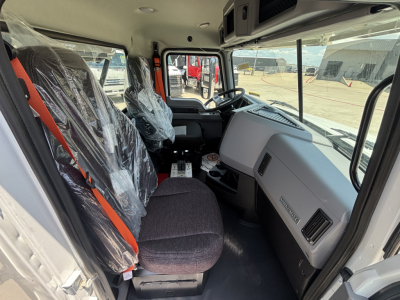 Truck cab interior of a new 2026 Mack GR64B roll-off truck showing steering wheel, dashboard, and front seats wrapped in plastic.