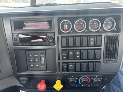 Dashboard interior of a 2026 Mack GR64B roll-off truck showing instrument cluster, switch panels, climate controls, and a radio unit.