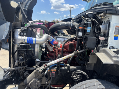 Mack GR64B engine bay showing high-compression diesel engine, hoses, and labeled fluid reservoirs in a new rolloff truck.