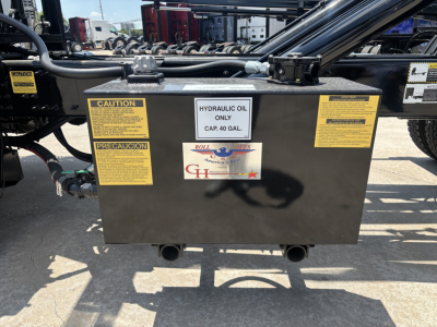 Black rectangular hydraulic oil reservoir with yellow caution and precaution labels on sides, capped at top, with two discharge pipes at bottom and a central white label reading HYDRAULIC OIL ONLY CAP. 40 GAL. and Roll Offs logo.