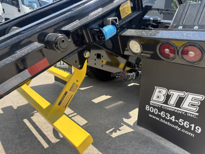 Mack GR64B roll-off truck chassis showing yellow support leg and hydraulic components with BTE Body Company branding visible on the side.
