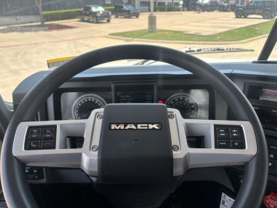 Steering wheel and dashboard of a Mack truck cab showing the Mack logo; instrument cluster and control buttons visible.