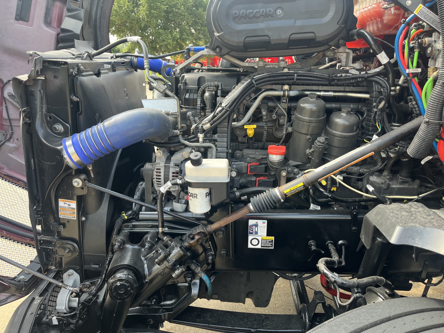Kenworth T680 engine bay with blue intercooler hose, coolant reservoir, various hoses, and intake components visible.
