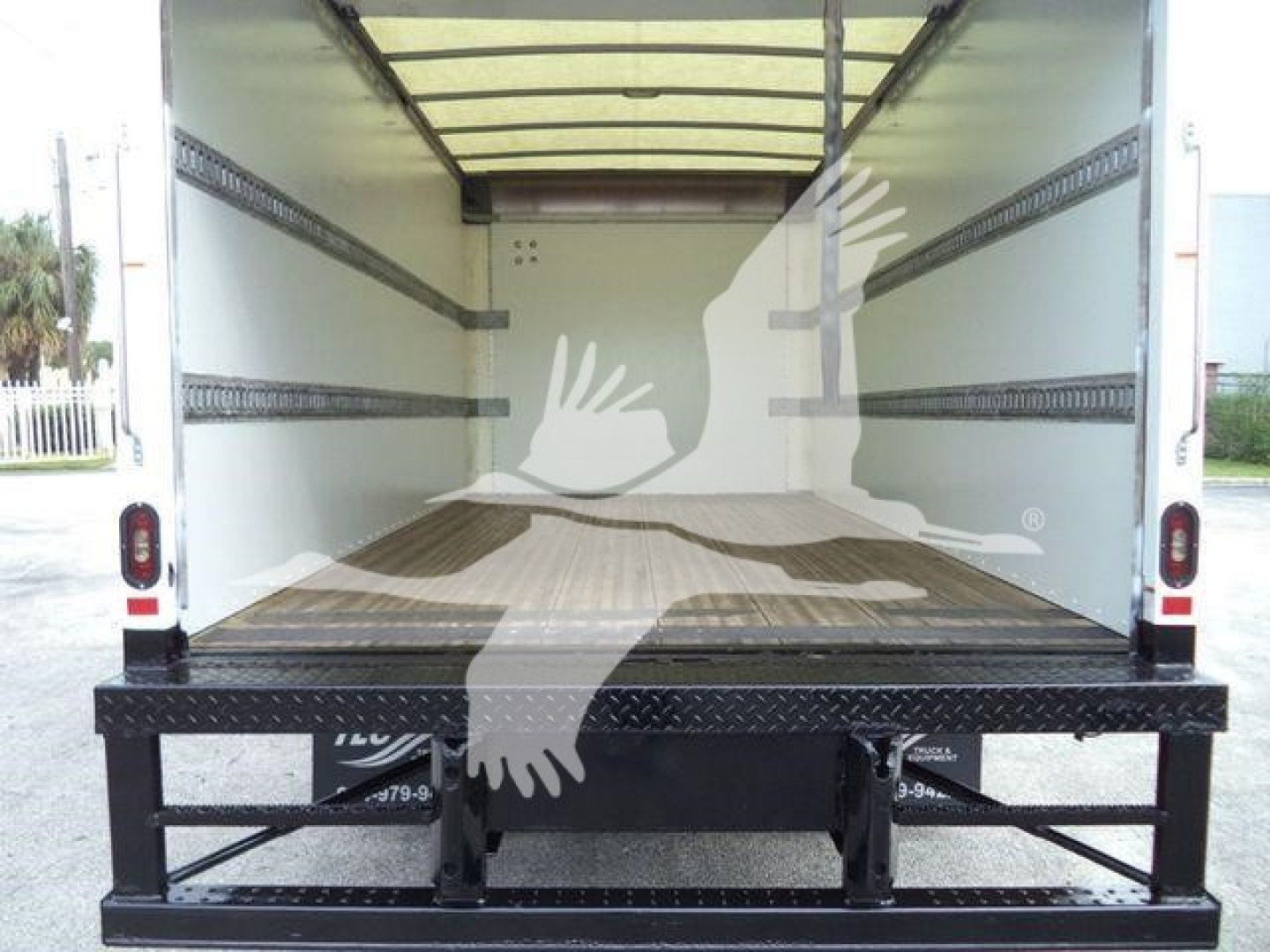 Isuzu NPR-HD box truck cargo area with empty interior and side wall rails; rear tail with ramp platform visible.