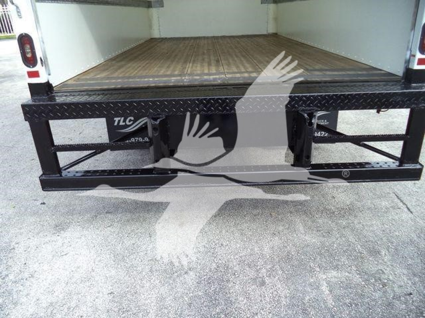 Isuzu NPR HD box truck rear view showing open cargo area and black steel ramp with TLC markings.