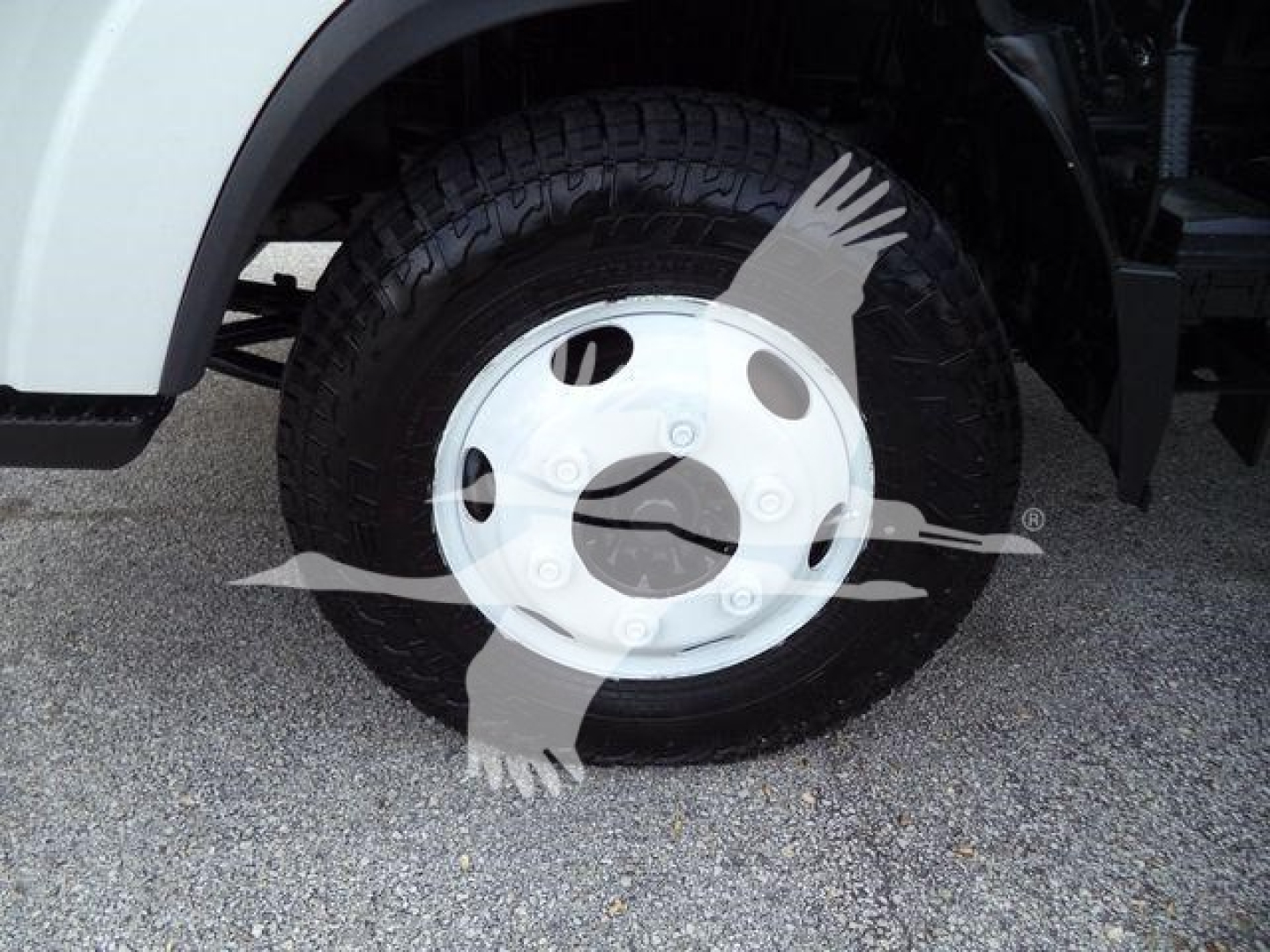 Isuzu NPR HD truck front wheel showing white steel wheel cover and tire; partial fender and suspension visible.