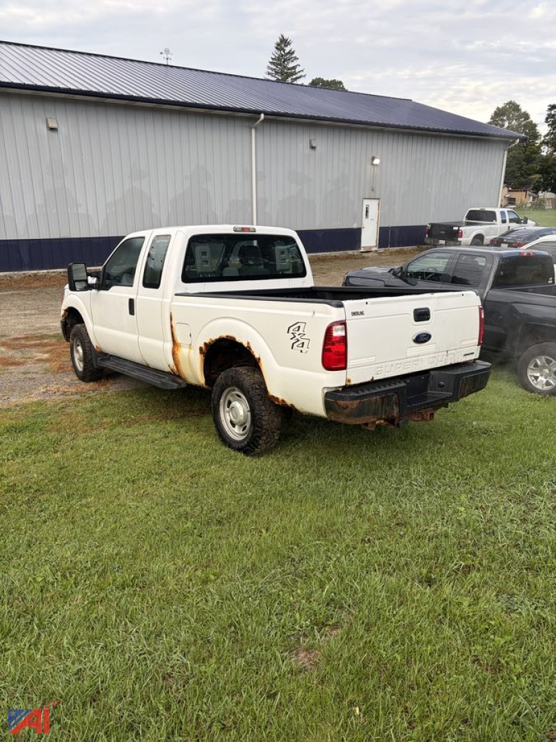 Ford F-350 Super Duty pickup with a crew cab and long bed, white, showing rust near wheel well, rear view of the truck bed, in a grassy lot.
