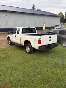 Ford F-350 Super Duty pickup with a crew cab and long bed, white, showing rust near wheel well, rear view of the truck bed, in a grassy lot.