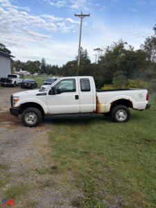 White 2016 Ford F-350 Super Duty pickup with extended cab, single rear wheel, visible rust along lower door and bed, profile view in a grassy lot.