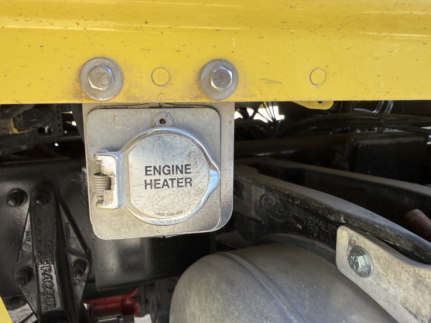 Truck engine bay showing the metal engine heater cover with the label ENGINE HEATER and surrounding components.