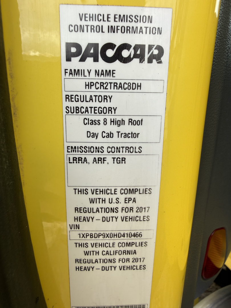 Vehicle emission control information label on a yellow surface. Text includes PACCAR, FAMILY NAME HPCR2TRAC8DH, REGULATORY SUBCATEGORY Class 8 High Roof Day Cab Tractor, EMISSIONS CONTROLS LRRA, ARF, TGR, THIS VEHICLE COMPLIES WITH US EPA R