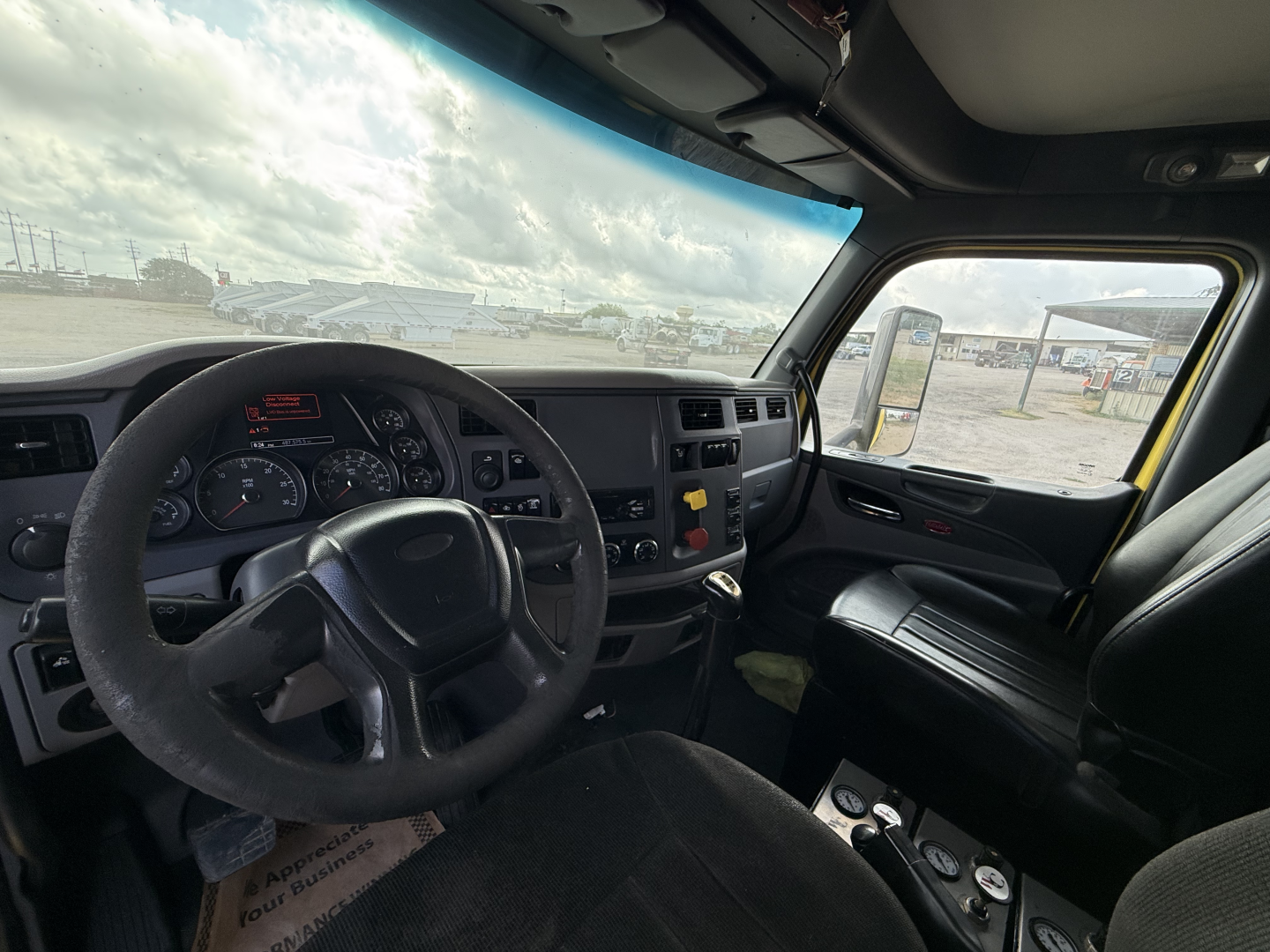 Truck cab interior of a Peterbilt 579 showing the steering wheel, dashboard, and driver's seat with controls; windshield and side window visible.