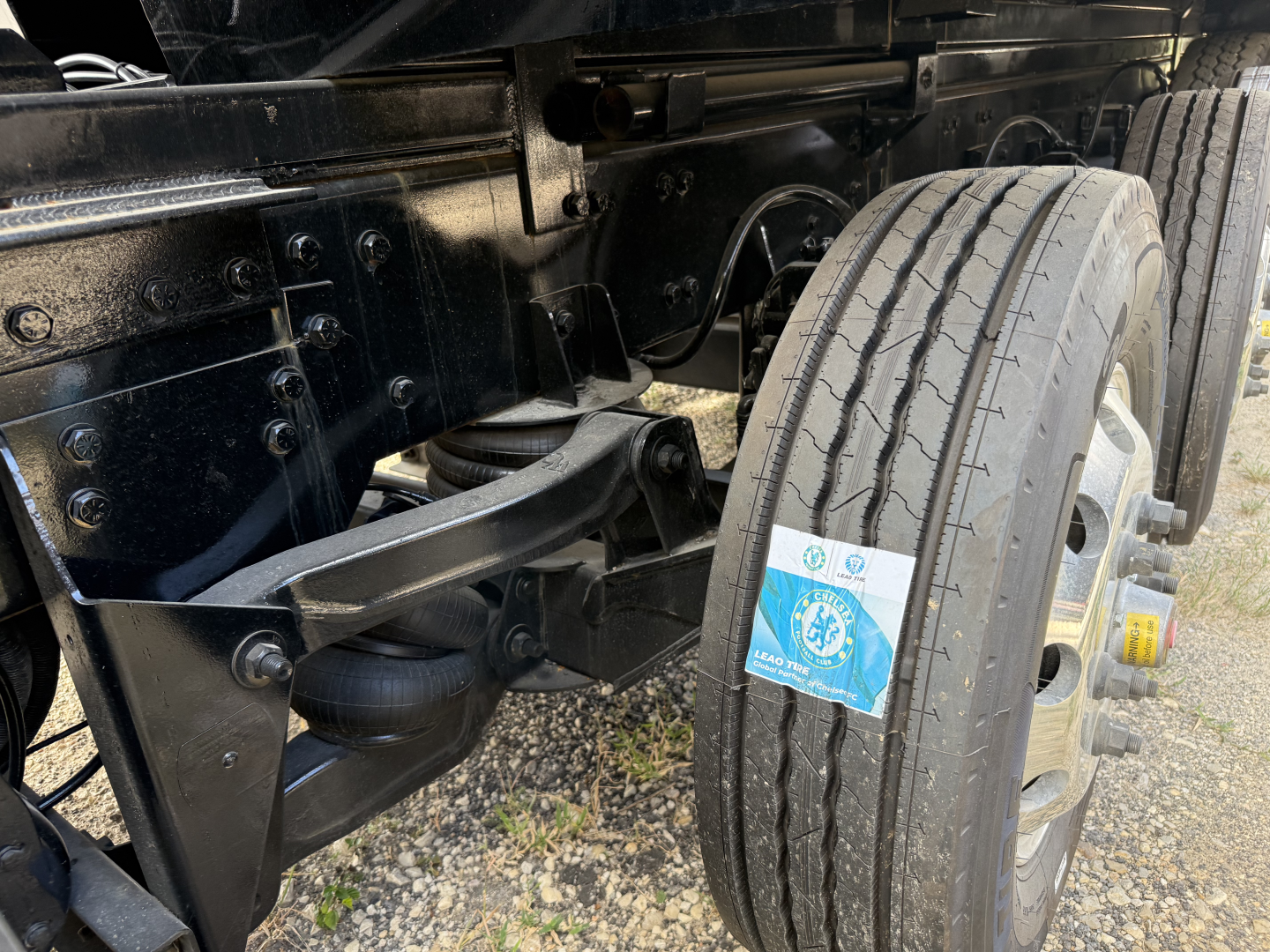 Peterbilt 579 chassis with dual rear wheels and front steering, undercarriage view showing suspension and wheel, with a blue inspection tag on the front tire.