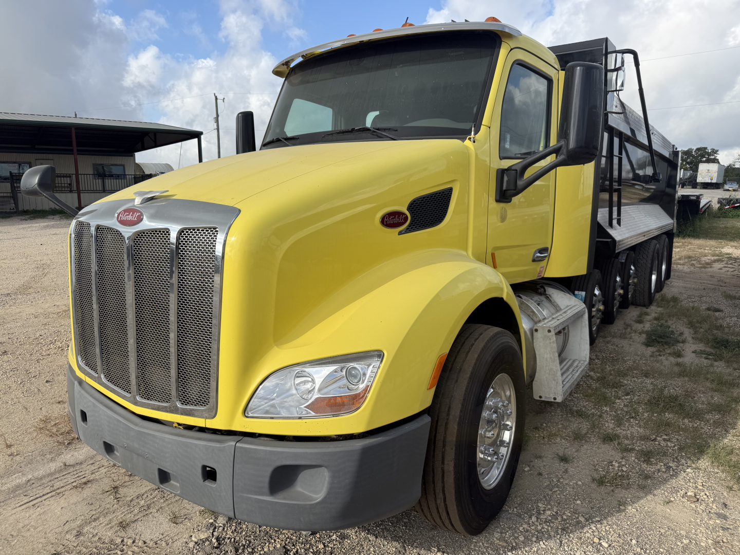 Yellow Peterbilt 579 dump truck cab front-right view with chrome grille and dual rear axles, VIN plate not visible.