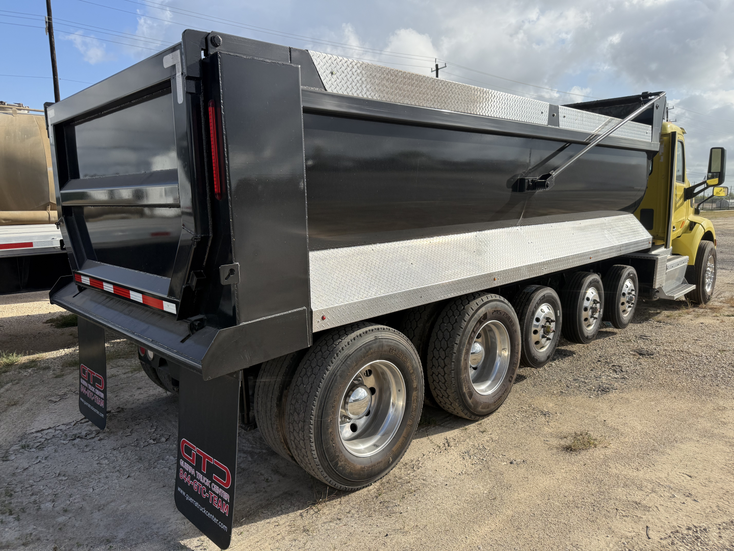 Peterbilt 579 dump truck side view showing multiple rear axles and dump bed with black panels and diamond plate side rails.