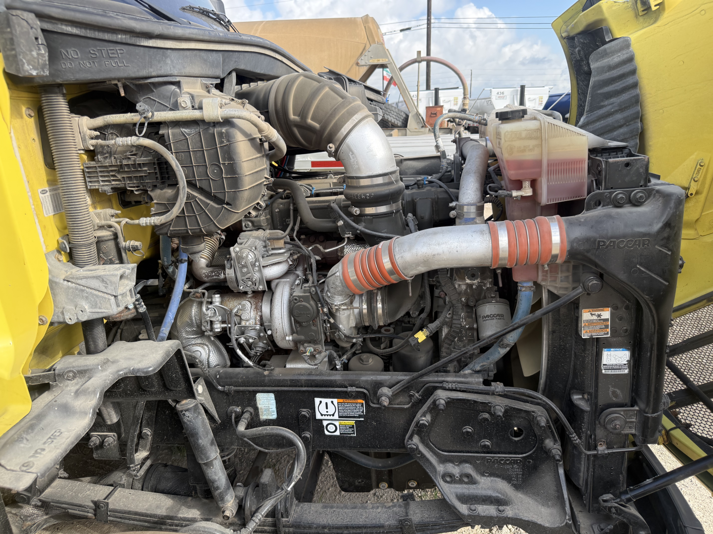 Engine bay of a 2017 Peterbilt 579 dump truck showing intercooler hose, air intake, radiator area, coolant reservoir, and various hoses with engine block visible.