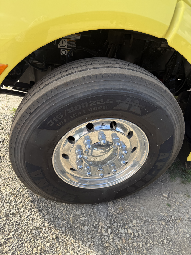 Truck wheel close-up showing Goodyear tire with size 315/80R22.5 and chrome hub, part of a yellow Peterbilt 579 dump truck.