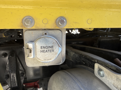 Truck engine bay showing the metal engine heater cover with the label ENGINE HEATER and surrounding components.