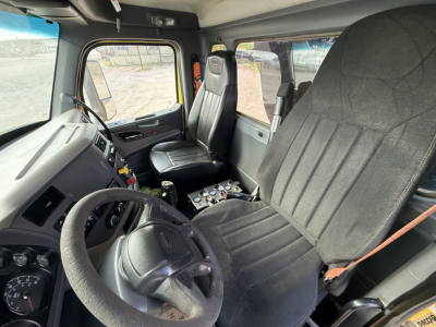Cab interior of a Peterbilt 579 dump truck showing steering wheel, driver's seat, passenger seat, dashboard controls, and window view.