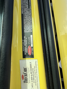 Label on yellow Peterbilt truck showing vehicle identification and care information, with stickers including Peterbilt and TrucCare branding.
