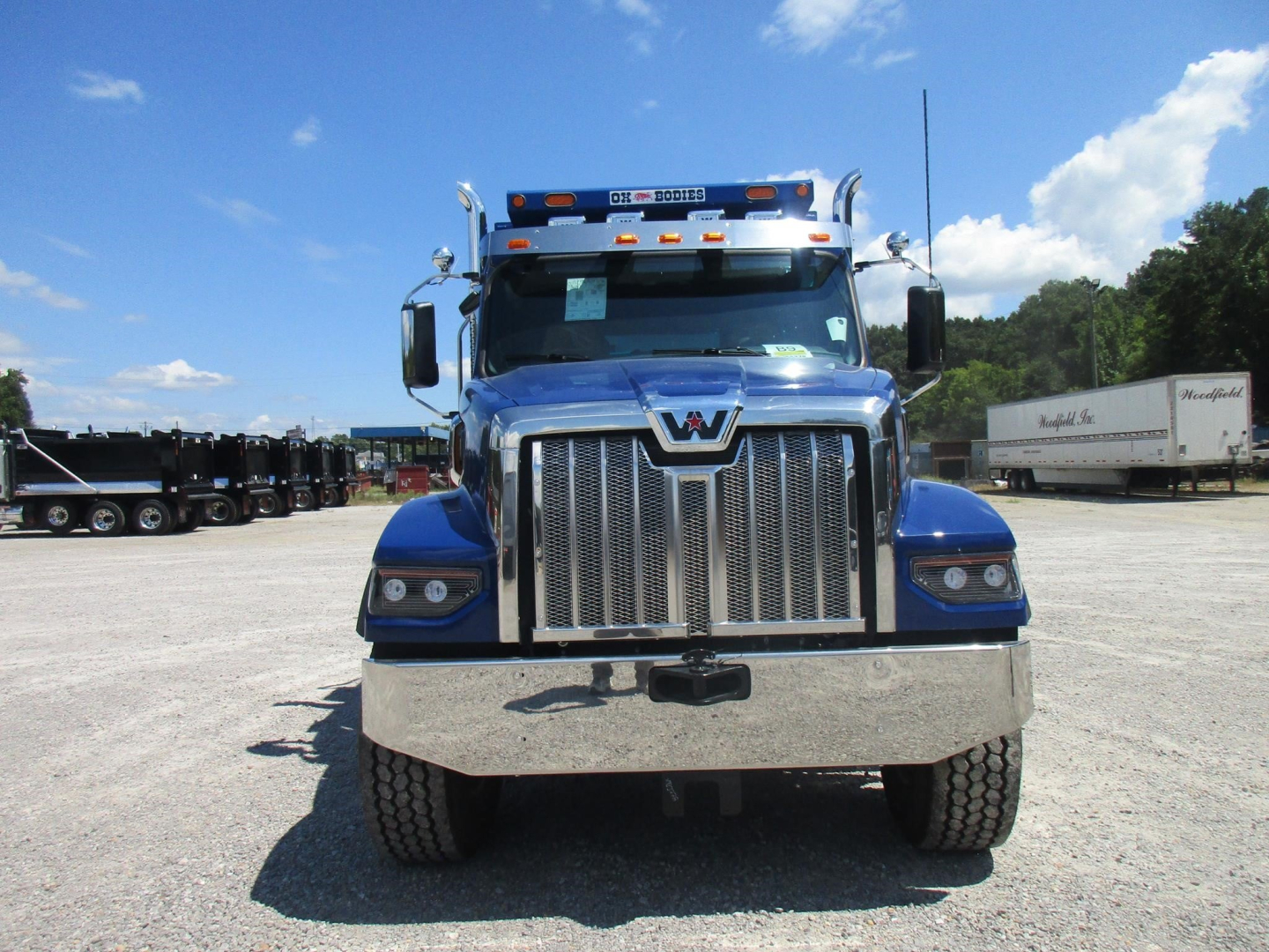 Front view of a blue Western Star 49X dump truck with chrome grille, headlights, and bumper, parked in a lot.