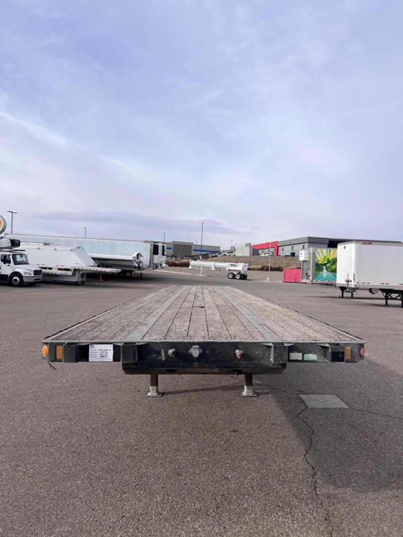 2014 Fontaine closed tandem w slider steel flatbed trailer viewed from front, showing wooden deck, undercarriage, and stabilizing legs.