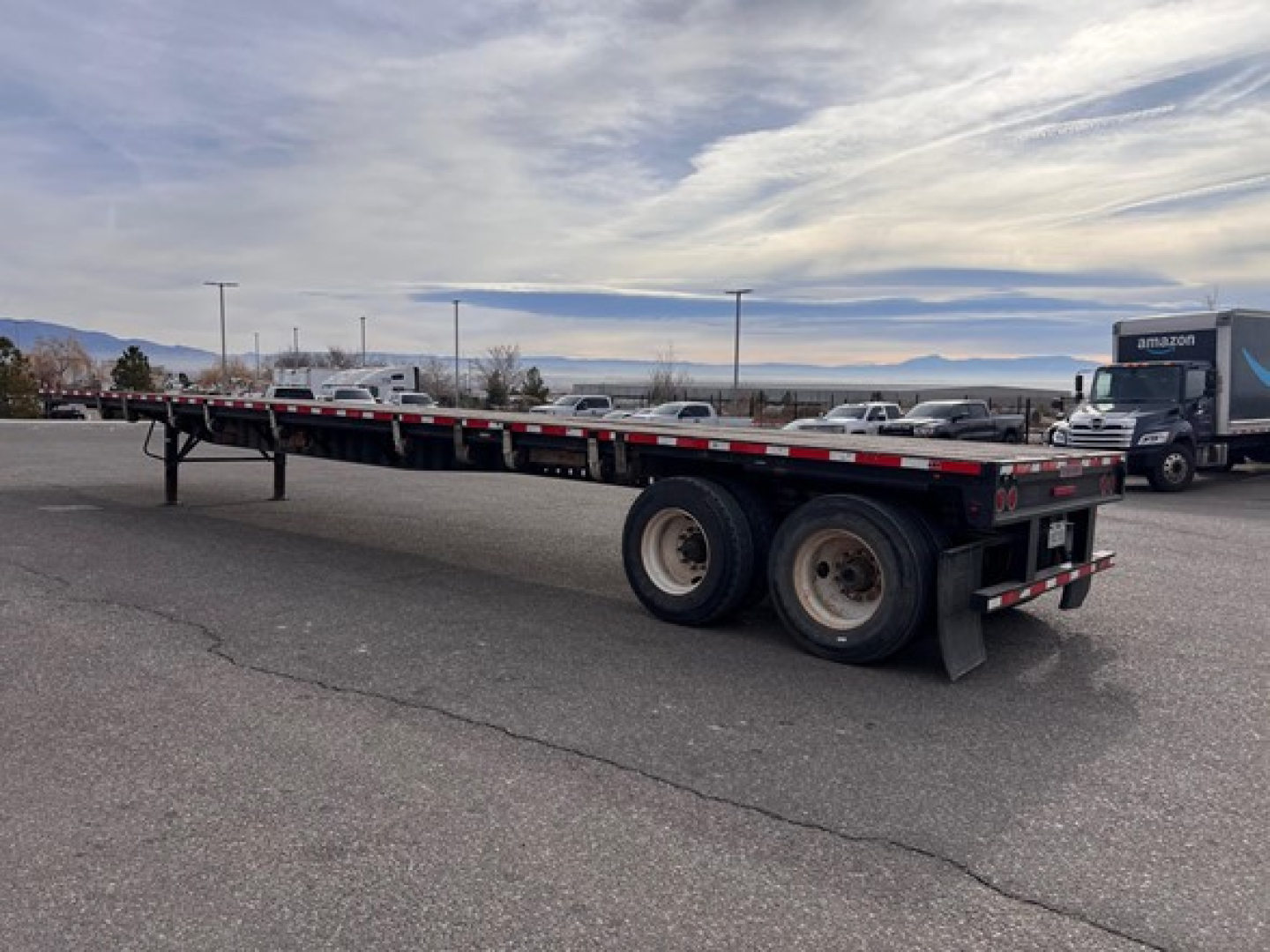 Flatbed trailer with tandem axles and slider steel flatbed showing side rails and rear lights.